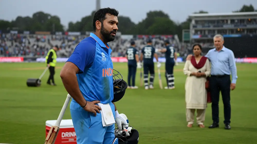 Cricket batter in blue kit playing a front-foot shot under stadium lights with a blurred crowd behind